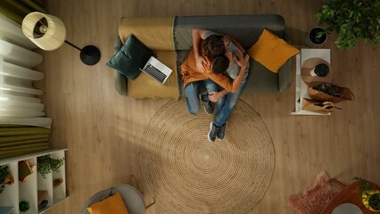 Top view shot of a homosexual couple at home. They are sitting on the couch and hugging. One of...
