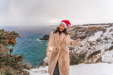 Outdoor winter portrait of happy smiling woman, light faux fur coat holding heart sparkler, posing...