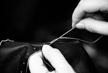 hands sew and mend the piece of leather with black and white effect