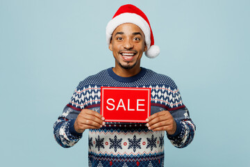 Young man wear knitted sweater Santa hat posing hold in hand card sign with sale title text...