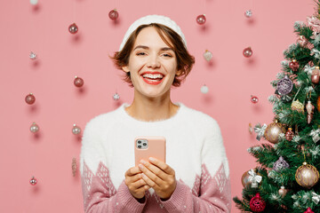 Merry smiling cool young woman wear white sweater hat posing hold in hand use mobile cell phone...