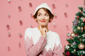 Merry young woman wear white sweater hat posing put hand prop up on chin, lost in thought and...