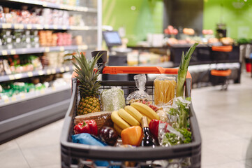 Full trolley cart of healthy fresh organic fruit vegetable goods shopping at modern supermaket store grocery shop buying choosing products inside hypermarket concept. Purchasing food, gastronomy.