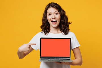 Young amazed IT woman wear white blank t-shirt casual clothes hold use work point finger on blank screen workspace area laptop pc computer isolated on plain yellow orange background Lifestyle concept