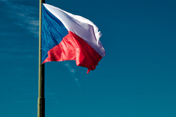 A photo of the Czech Republic flag flying on a flagpole against a blue sky.