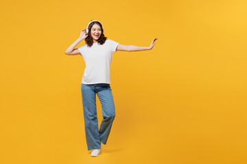 Fototapeta na wymiar Full body young smiling cool woman wear white blank t-shirt casual clothes listen to music in headphones dance have fun isolated on plain yellow orange background studio portrait. Lifestyle concept.
