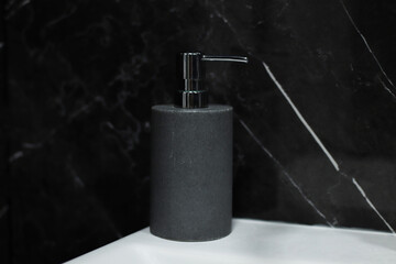 Stylish gray ceramic liquid soap bottle on a white sink in a dark style bathroom. Concept of...