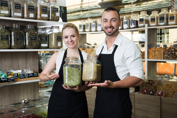 Pair of charming sellers with aprons at store of herbs and ecological food