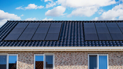 Fototapeta premium Black solar panels attached to the roof against a sunny sky Close up of new building with black solar panels. Zonnepanelen, Zonne energie, Translation: Solar panel, Sun Energy in the Netherlands