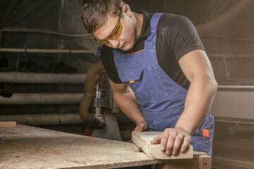 Close-up as a young man gray t-shirt by profession carpenter builder equals a wooden bar milling machine on a wooden table in the workshop