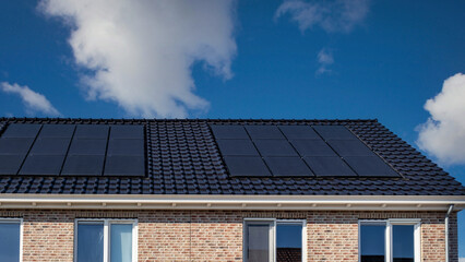 Newly built houses with solar panels attached on the roof against a sunny sky, Close up of new building with black solar panels. Zonnepanelen, Zonne energie, Translation: Solar panel, Sun Energy - obrazy, fototapety, plakaty