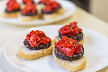 Black pudding tapa from Burgos with roasted peppers, presented on a slice of bread and decorated with peppers