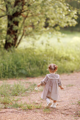 Super cute anonymous blonde with curly hair in a white dress walking along a rural road. Small...