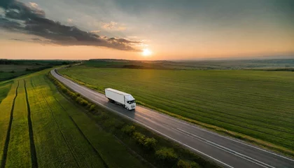 Poster white truck driving on asphalt road along the green fields at sunset seen from the air aerial view landscape drone photography cargo delivery © Enzo