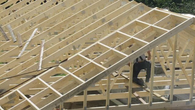 A roofing carpenter works to install the roof of an unfinished house. Building a house.