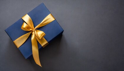 dark blue gift box with gold satin ribbon on dark background top view of birthday gift with copy space for holiday or christmas present
