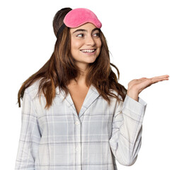 Young Caucasian woman in pajamas with mask showing a copy space on a palm and holding another hand on waist.