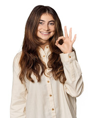 Young Caucasian woman in studio setting cheerful and confident showing ok gesture.