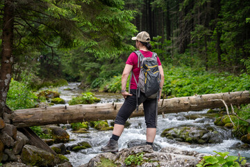 Naklejka na ściany i meble a woman on a mountain hike stops by a stream and looks where to go next