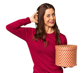 Middle-aged woman with Valentine's Day heart box in studio touching back of head, thinking and making a choice.