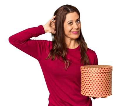Middle-aged woman with Valentine's Day heart box in studio touching back of head, thinking and making a choice.