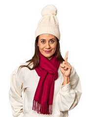 Middle-aged woman in cozy Christmas winter wear in studio showing number one with finger.