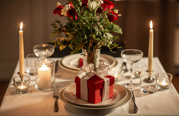 holidays, romantic date and celebration concept - close up of festive table serving for two with gift box, flowers in vase and candles burning at home on valentine's day