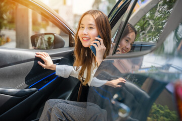 Confidence and technology blend as an Asian businesswoman sits in her car, talking on the phone. She's poised for success, with the open car door representing her active role in the business world. - Powered by Adobe