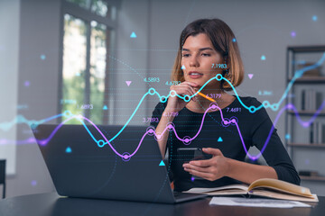 Pensive attractive beautiful businesswoman in working on laptop, talking phone, office workplace in background. Forex graph and charts hologram icons. Concept of market trading and research.