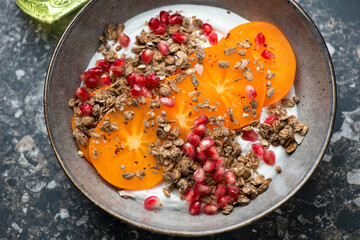 Grey plate with greek yogurt, sliced persimmon, granola and pomegranate, middle close-up, horizontal shot