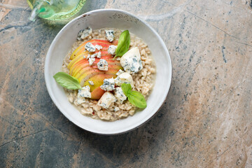 Grey bowl with pear and blue cheese risotto, top view on a beige and grey granite background, horizontal shot with space