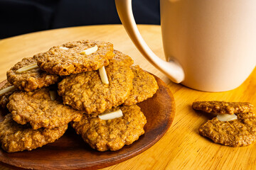 Pile of crispy delicious homemade coconut cookies in wooden plate with pink ceramic coffee cup on wooden board.