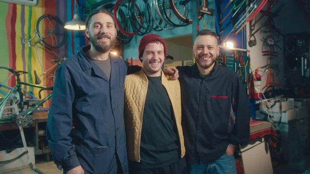 Team of young cheerful mechanics standing together in bicycle workshop, smiling and posing on camera. Group portrait, zoom shot