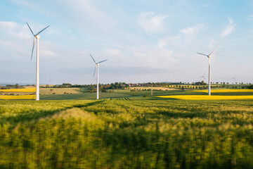 Countryside landscape with flowering rapeseed field with wind power turbines in the sunny day in...