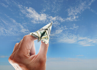Hand holding an origami dollar paper airplane with blue sunny sky -- financial goal investing concept