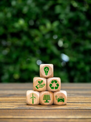 Eco friendly, green renewable energy icons on wooden cube block stack pyramid shape on green leaves background, vertical style. Environmental sustainability, Net zero carbon dioxide reduction concept.