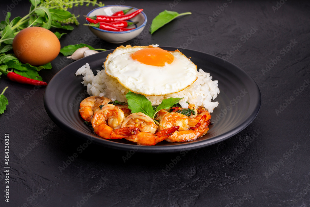 Poster stir-fried shrimp with basil thai street food arranged on a black plate with a fried egg thai spicy 