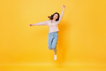 Cheerful Asian woman in casual clothes smiling and jumping with hands up in colorful yellow color...