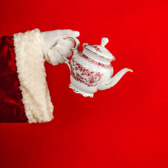 Santa's Hand holding porcelain teapot on bright red background with copy space.