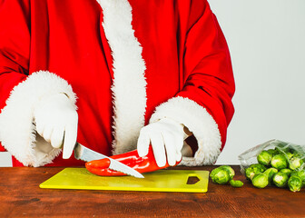 Santa Claus in traditional costume prepares red sweet paprika and broccoli. Healthy eating and cooking. Holiday food.