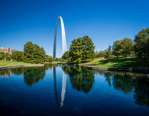 View across blue lake in the National Gateway Park to Gateway Arch in St Louis Missouri with reflection in the calm water - obrazy, fototapety, plakaty