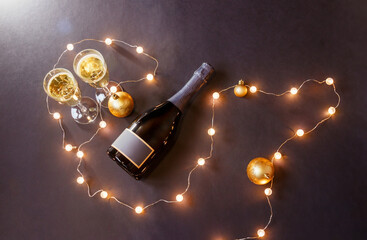 Glasses of champagne, bottle of champagne, christmas balls and glowing christmas lights on dark background.