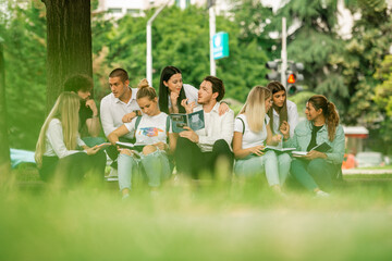Multiracial young group of university or high school students sitting together outside on the sidewalk talking to each other laughing and studying