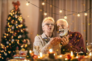 A jolly senior couple is celebrating christmas and new year's eve at home with confetti.