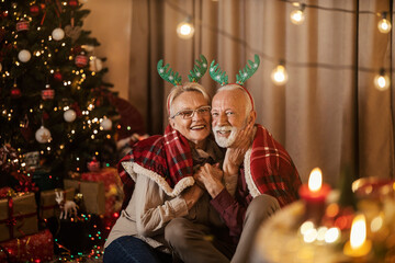 A jolly senior couple is hugging and celebrating christmas and new year's eve at home.
