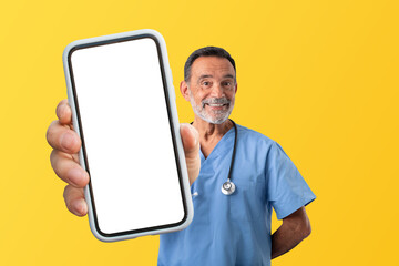 Mature medical worker man in uniform demonstrating smartphone screen, studio