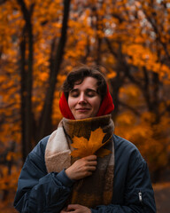 girl in the park with a maple leaf in a bomber jacket and a red hood shut eys smiling scarf