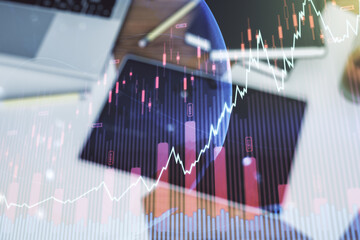 Abstract creative financial graph with world map and modern digital tablet on background, top view, forex and investment concept. Multiexposure