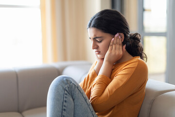 Upset young woman sitting on couch and covering her ears with hands