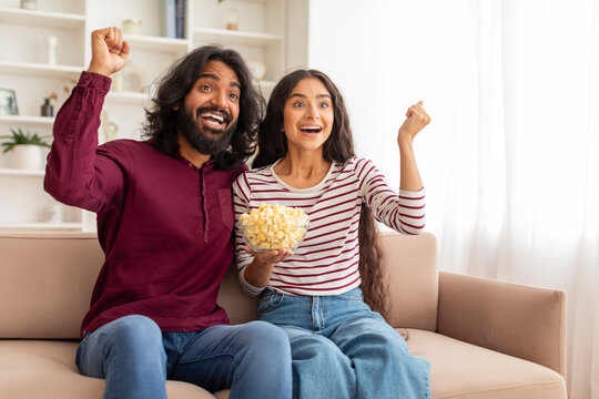 Thrilled indian couple watching football match at home